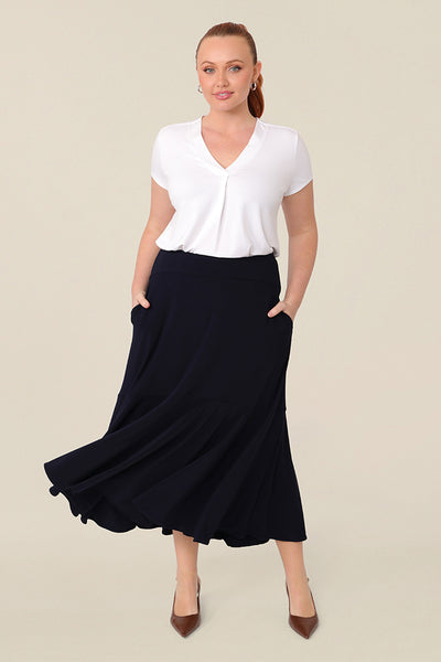A woman wears a pull on, navy maxi skirt with ruffle hemline with a short sleeve bamboo jersey top in white. This black maxi skirt is a good workwear skirt or smart-casual skirt. Made in Australia in petite plus sizes for all curve of women's bodies..