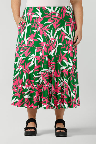 A size 18 woman wears a green jersey skirt with a leaf print. On a verdant green base in a soft jersey fabric. Styled back with black platforms. Made in Australia for women size 8 - 24.