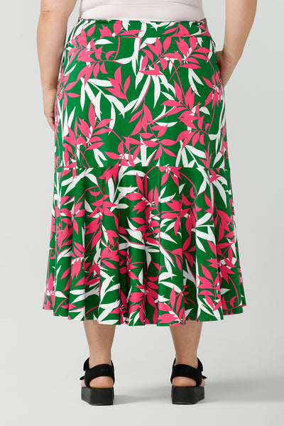 A size 18 back view of a woman wearing a green jersey skirt with a leaf print. On a verdant green base in a soft jersey fabric. Styled back with black platforms. Made in Australia for women size 8 - 24.