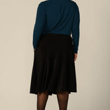 Back view of a fuller figure woman wearing a pull on, black skirt with knee-length ruffle hem and side pockets. This black skirt is a comfortable skirt for work wear or smart-casual wear.