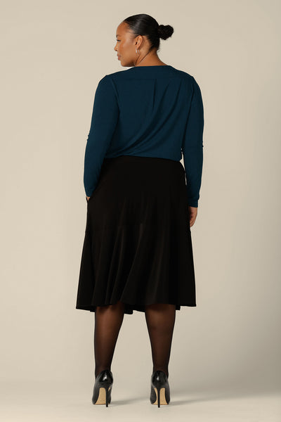 Back view of a fuller figure woman wearing a pull on, black skirt with knee-length ruffle hem and side pockets. This black skirt is a comfortable skirt for work wear or smart-casual wear.