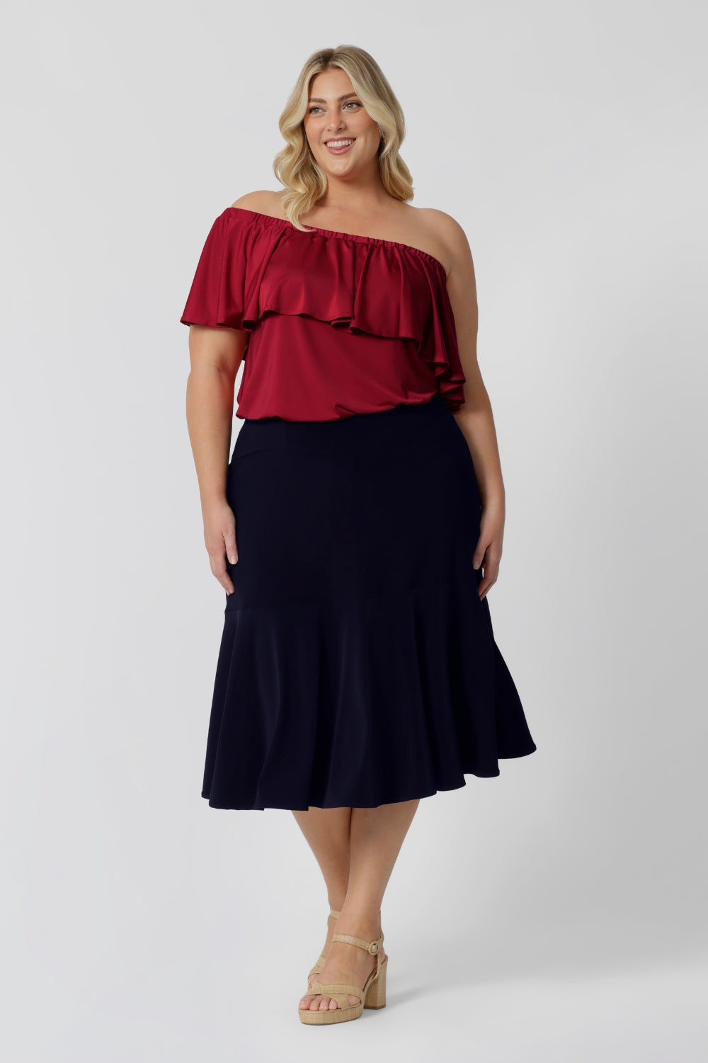 a size 18, fuller figure woman wears a knee-length, navy blue jersey skirt with ruffle hem. The skirt is worn with a white, long sleeve, bamboo jersey top for a smart-casual look that translates for easy work wear style.