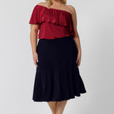 a size 18, fuller figure woman wears a knee-length, navy blue jersey skirt with ruffle hem. The skirt is worn with a white, long sleeve, bamboo jersey top for a smart-casual look that translates for easy work wear style.