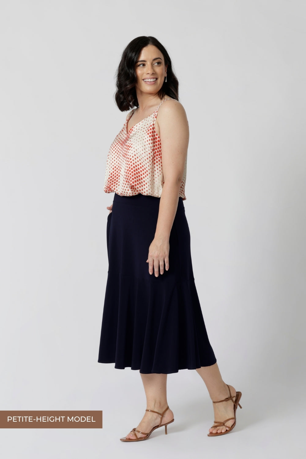 A navy blue, below-the-knee-length skirt with ruffle hemline. A pull-on skirt in stretch jersey fabric, this is a comfortable skirt for all-day work wear. Petite height model wears navy workwear skirt with matching summer ready cami.