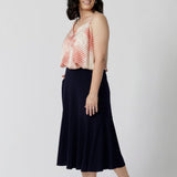 A navy blue, below-the-knee-length skirt with ruffle hemline. A pull-on skirt in stretch jersey fabric, this is a comfortable skirt for all-day work wear. Petite height model wears navy workwear skirt with matching summer ready cami.