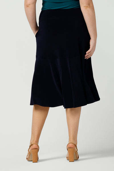Back view of an Australian-made skirt by New Zealand and Australian women's clothing brand, Leina & Fleur. This navy blue knee-length skirt in comfortable jersey fabric is shown in a size 12 as workwear for curvy women. Available from their online boutique in Australia, this classic navy skirt is available as petite to plus size office wear thanks to their size range of sizes 8, 10, 12, 14, 16, 18, 20, 22 and 24.