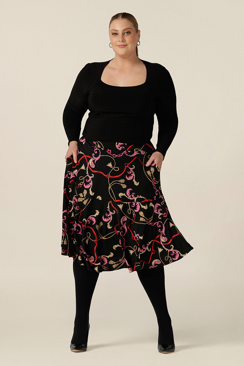 A curvy, size 18 woman wears a good skirt for plus size workwear. The Berit Skirt in Tassel is a pull-on knee length skirt with pockets and ruffle hem, and is worn with a square neck, long sleeve black top.  Both women's plus size skirt and top are made in Australia by Australian fashion brand, L&F.