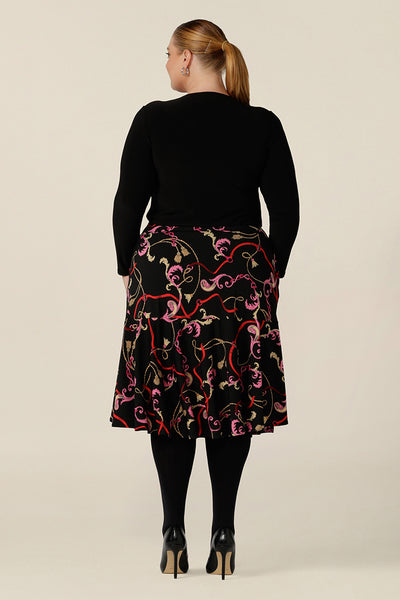 Back view of a curvy, size 18 woman wearing a good skirt for plus size workwear. The Berit Skirt in Tassel is a pull-on knee length skirt with pockets and ruffle hem, and is worn with a square neck, long sleeve black top. Both women's plus size skirt and top are made in Australia by Australian fashion brand, L&F.