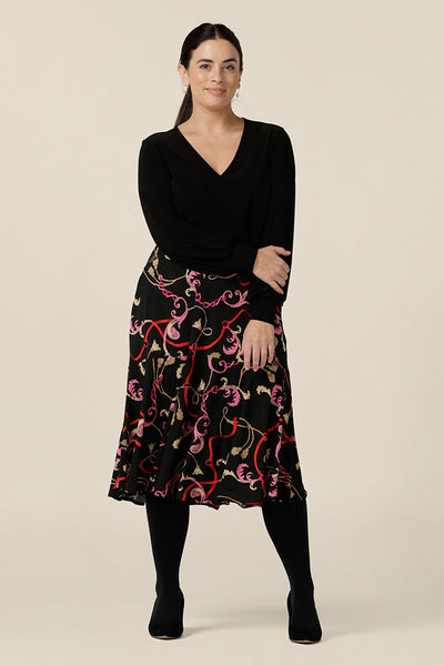 A woman wears a good workwear skirt in size 10. The Berit Skirt in Tassel is a pull-on knee length skirt with pockets and ruffle hem, and is worn with a V neck, long bishop sleeve black top. Both women's plus size skirt and top are made in Australia by Australian fashion brand, L&F.
