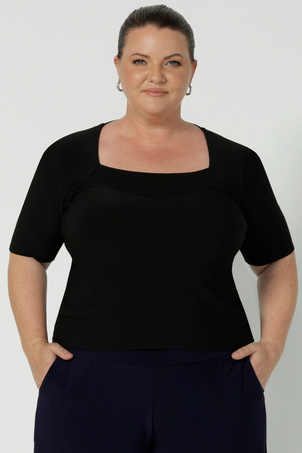 Close up of a curvy woman wears short sleeve black top with square neckline. A slim fit top in classic black, this tailored jersey top wears well with workwear separates for an office look and also as a smart casual top. Shop tops online at Australian women's clothing brand, Leina & Fleur n sizes 8-24.