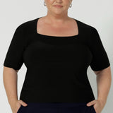 Close up of a curvy woman wears short sleeve black top with square neckline. A slim fit top in classic black, this tailored jersey top wears well with workwear separates for an office look and also as a smart casual top. Shop tops online at Australian women's clothing brand, Leina & Fleur n sizes 8-24.