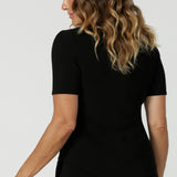 Back view close up of a curvy woman wears short sleeve black top with square neckline. A slim fit top in classic black, this tailored jersey top wears well with workwear separates for an office look and also as a smart casual top. Shop tops in petite, mid size and plus size online at Australian women's clothing brand, Leina & Fleur.