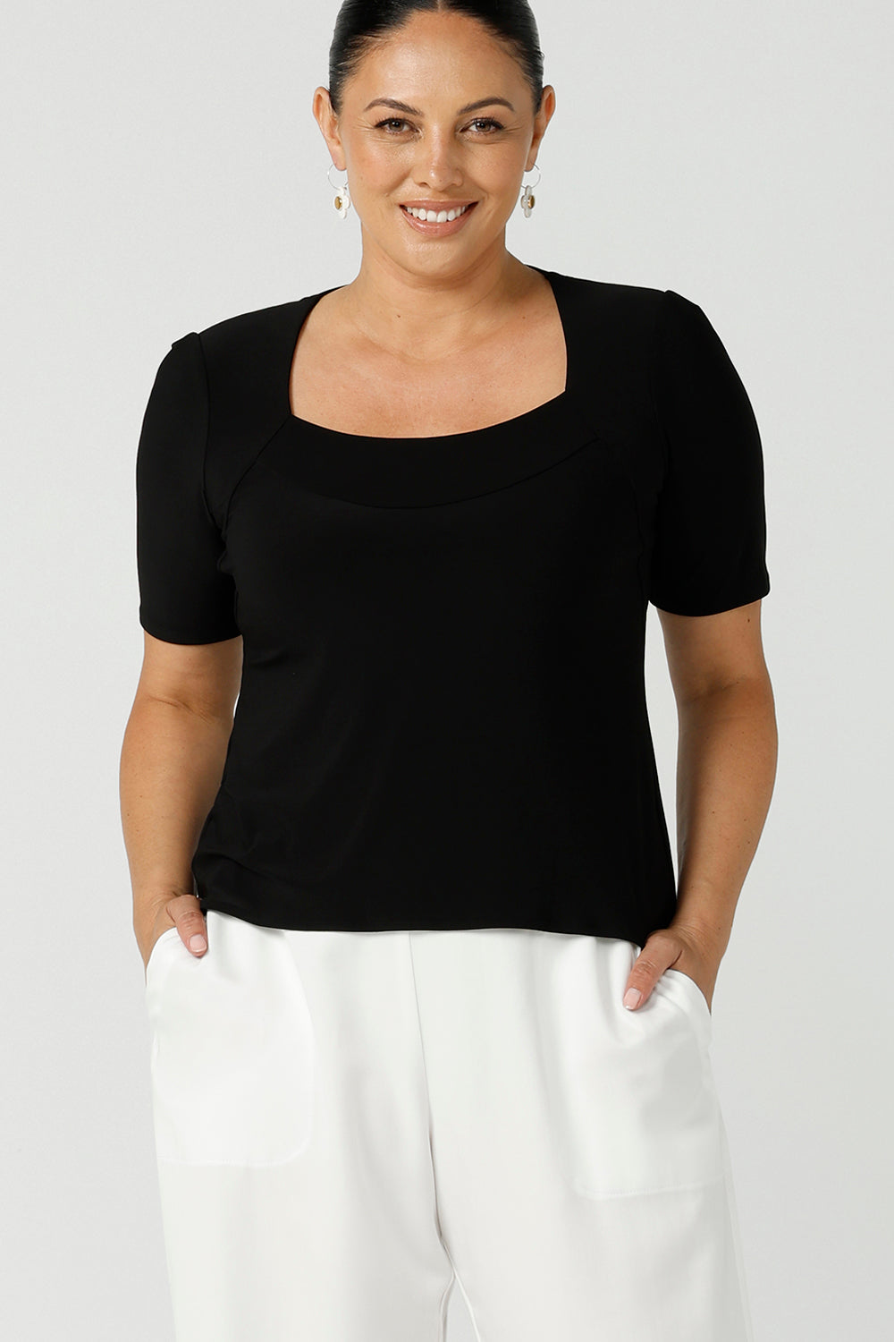 Close up of a curvy woman wears short sleeve black top with square neckline. A slim fit top in classic black, this tailored jersey top wears well with workwear separates for an office look and also as a smart casual top. Shop tops in petite, mid size and plus size online at Australian women's clothing brand, Leina & Fleur.