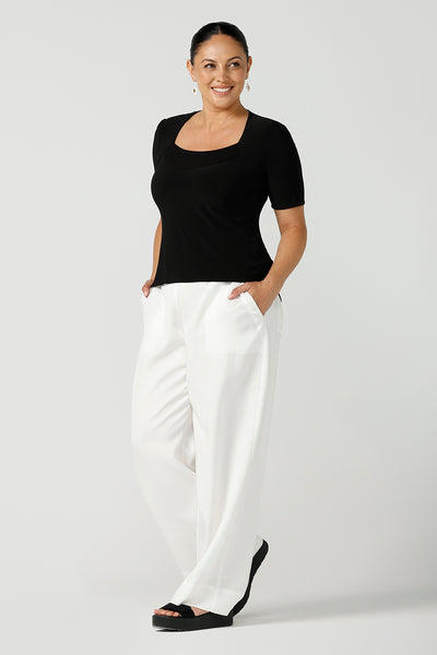 A curvy woman wears short sleeve black top with square neckline. A slim fit top in classic black, this tailored jersey top wears well with workwear separates for an office look and also as a smart casual top. Shop tops in petite, mid size and plus size online at Australian women's clothing brand, Leina & Fleur.