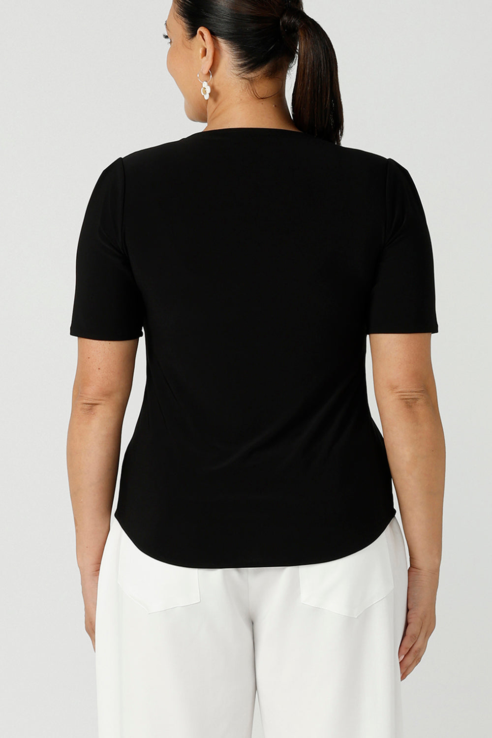 Back view close up of a curvy woman wears short sleeve black top with square neckline. A slim fit top in classic black, this tailored jersey top wears well with workwear separates for an office look and also as a smart casual top. Shop tops in petite, mid size and plus size online at Australian women's clothing brand, Leina & Fleur.