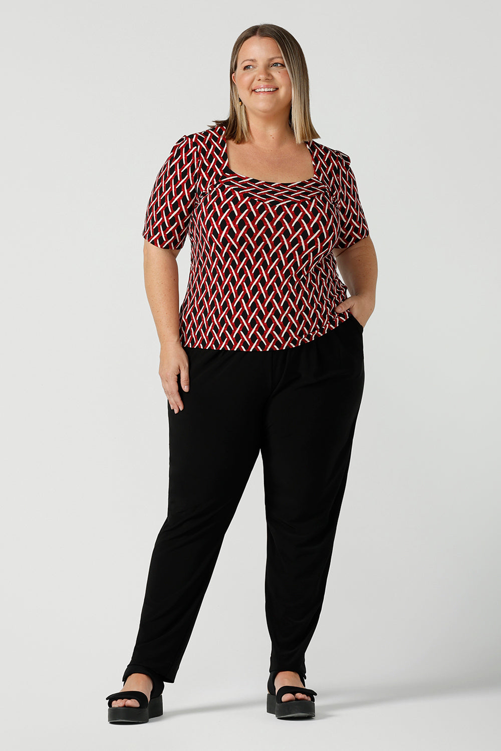 Curvy size 16 woman wears a geometric Chevron print Berni top. Corporate causal work wear top that is comfortable and versatile. Styled back with Black Indi pants. Made in Australia for women size 8 - 24.