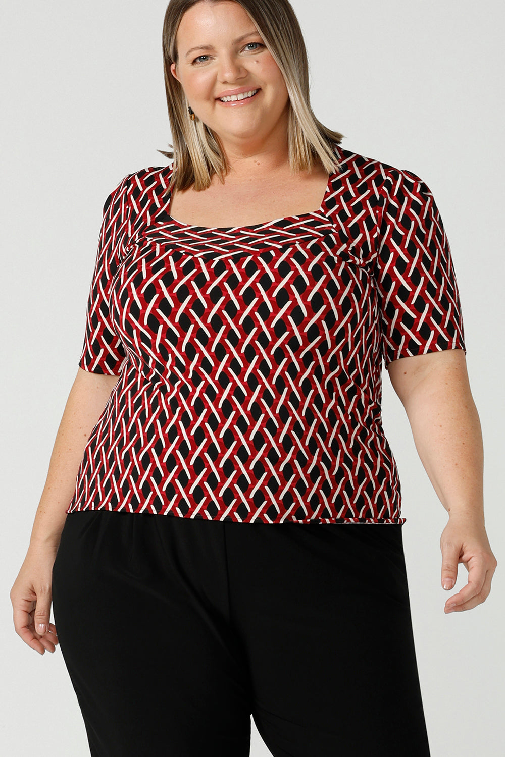Curvy size 16 woman wears a geometric Chevron print Berni top. Corporate causal work wear top that is comfortable and versatile. Styled back with Black Indi pants. Made in Australia for women size 8 - 24.
