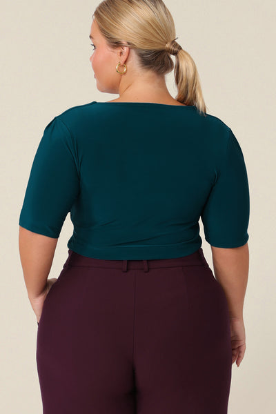 Back view of a size 14 curvy woman wearing a short-sleeve jersey top in dark teal. The top has a squared scoop neckline, a structured bust and short sleeves.  Wear for work or casual and shop in sizes 8 to size 24.