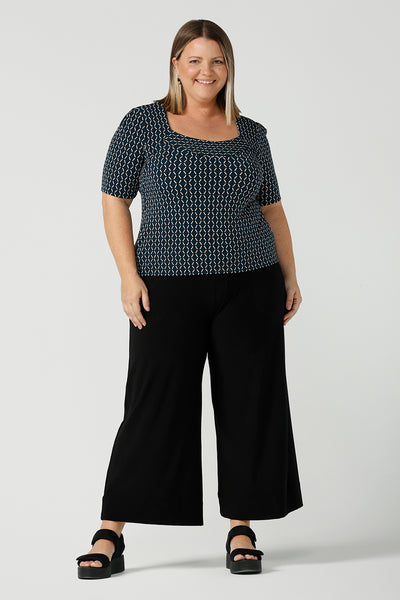 A plus size 16 woman wears the Berni Top in Infinity with a jade base colour and geometric pattern. A comfortable jersey work top style back with a wide leg Bradley pant. Made in Australia for women size 8 - 24.