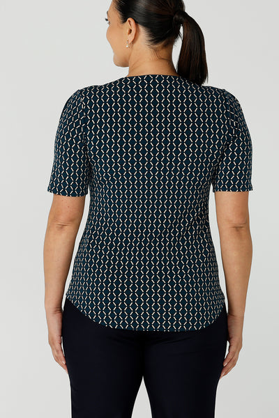 Back view of a curvy size 12 woman wears the Berni Top in Infinity with a jade base colour and geometric pattern. A comfortable jersey work top style back with the Lulu pants in navy. Made in Australia for women size 8 - 24.