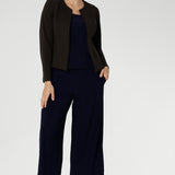 Size 10 woman wears a casual jersey top in navy blue. This Australian-made women's top has short fitted sleeves, a square neckline and and high-low - perfect for weekend casual and travel capsule wardrobes. Available in sizes 8-24. Styled with matching navy culottes & brown jacket