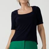 A size 10 over 40 year old woman wears a casual jersey top in navy blue, styled with emerald green pants. This Australian-made women's top has short fitted sleeves, a square neckline and and high-low - perfect for weekend casual and travel capsule wardrobes.