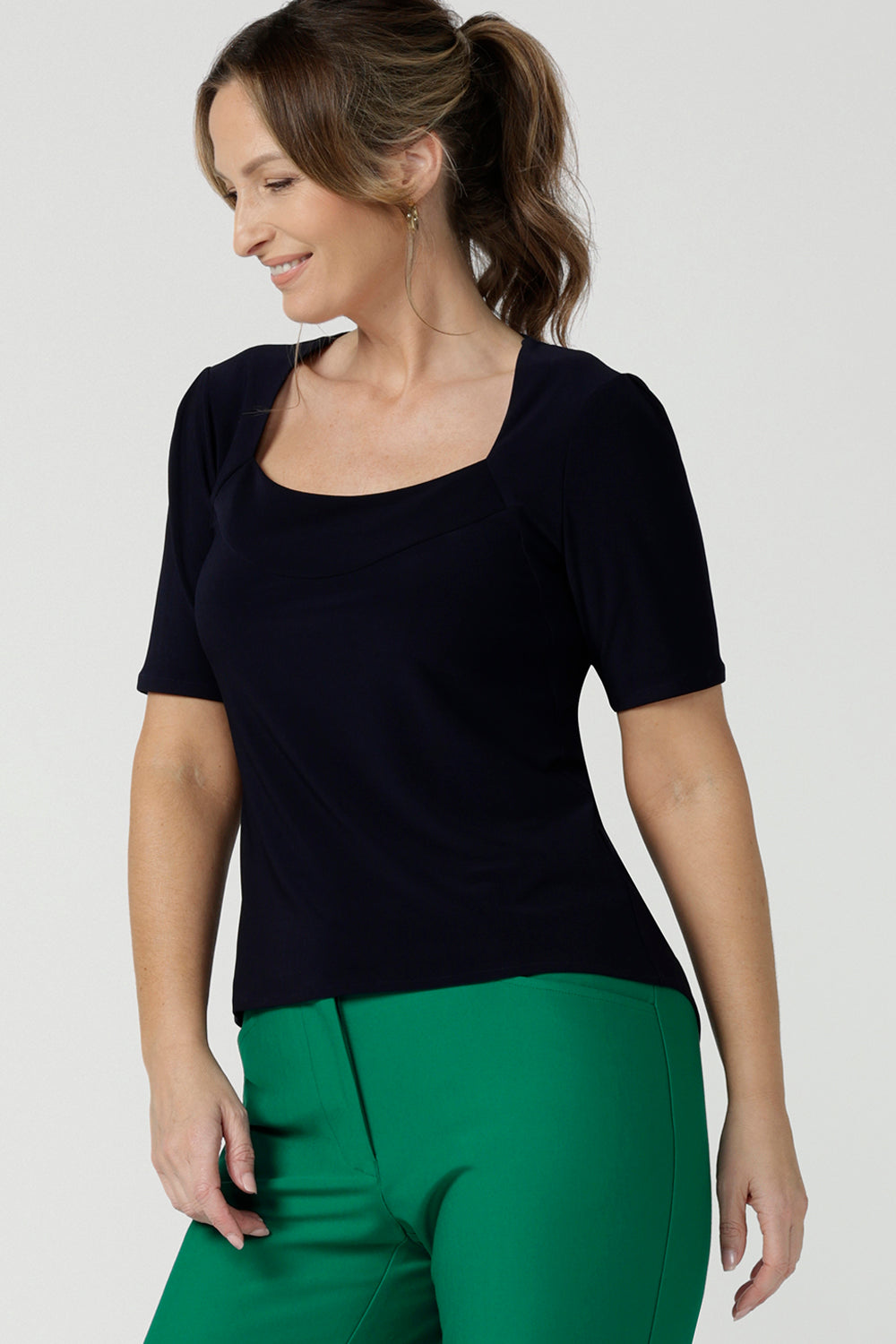 A size 10 over 40 year old woman wears a casual jersey top in navy blue, styled with emerald green pants. This Australian-made women's top has short fitted sleeves, a square neckline and and high-low - perfect for weekend casual and travel capsule wardrobes.