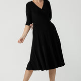 Size 10 woman wears the Bettina dress in black soft jersey. Wrap front reversible design with pockets and a tier. Styled back with black sling back shoes. Made in Australia for women size 8 - 24.