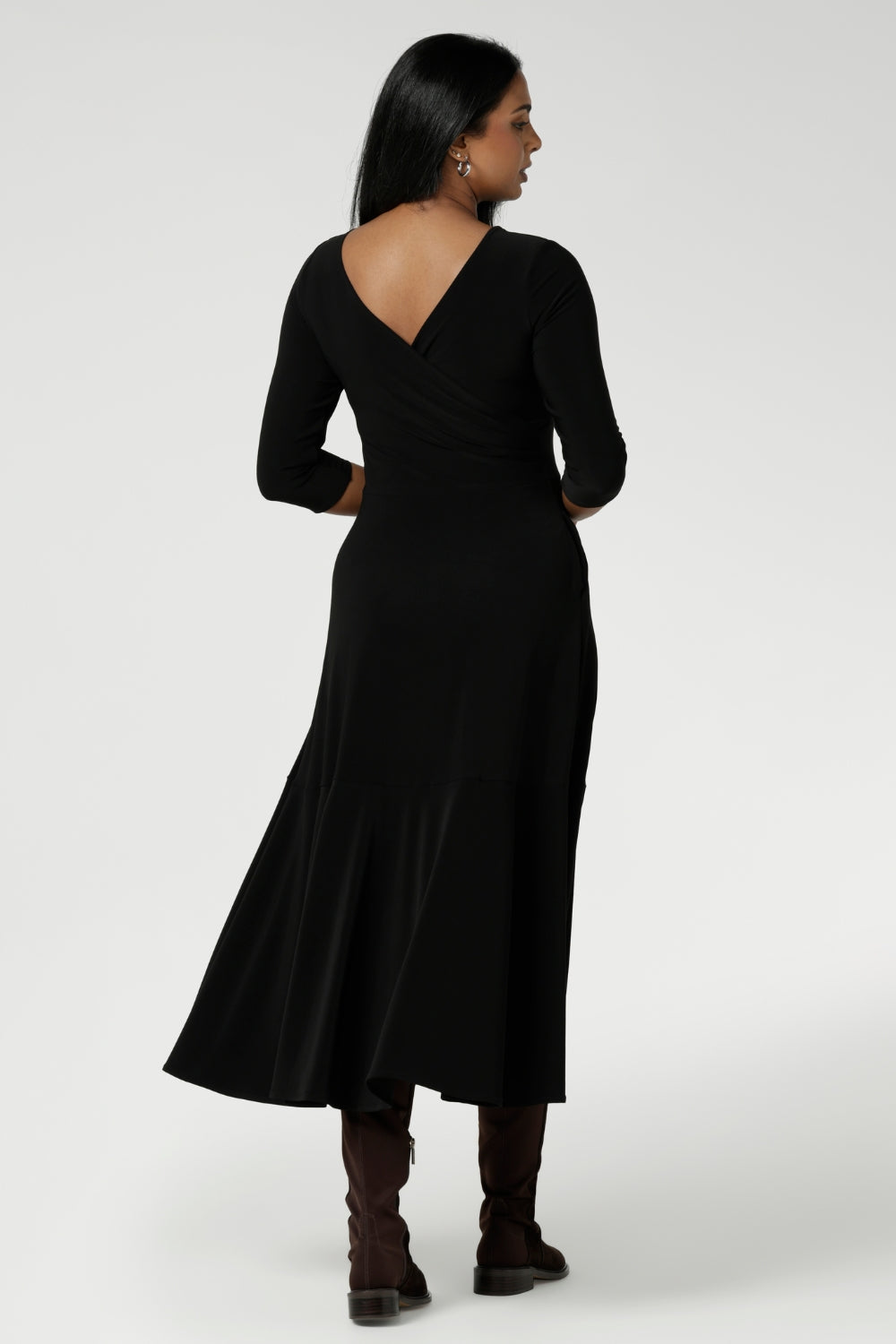 Size 10 woman wears Bettina Reversible Dress in Black. Australian made Jersey fixed wrap dress features a V-neck style with pockets and midi length. Made in Australia for plus size women and petite height women sizes 8-24. Dress worn with Vneckline back facing and styled with long boots.