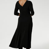 Size 10 woman wears Bettina Reversible Dress in Black. Australian made Jersey fixed wrap dress features a V-neck style with pockets and midi length. Made in Australia for plus size women and petite height women sizes 8-24. Dress worn with Vneckline back facing and styled with long boots.