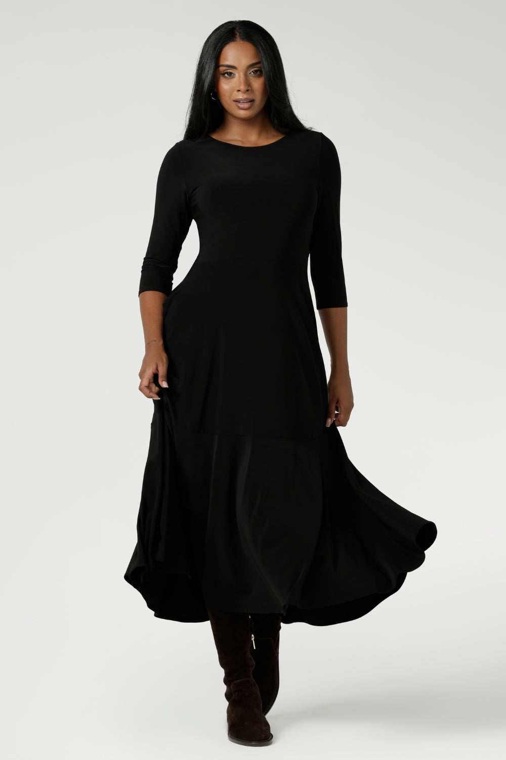 Size 10 woman wears Bettina Reversible Dress in Black. Australian made Jersey fixed wrap dress features a V-neck style with pockets and midi length. Made in Australia for plus size women and petite height women sizes 8-24. Dress worn with boat neck front facing and styled with long boots.