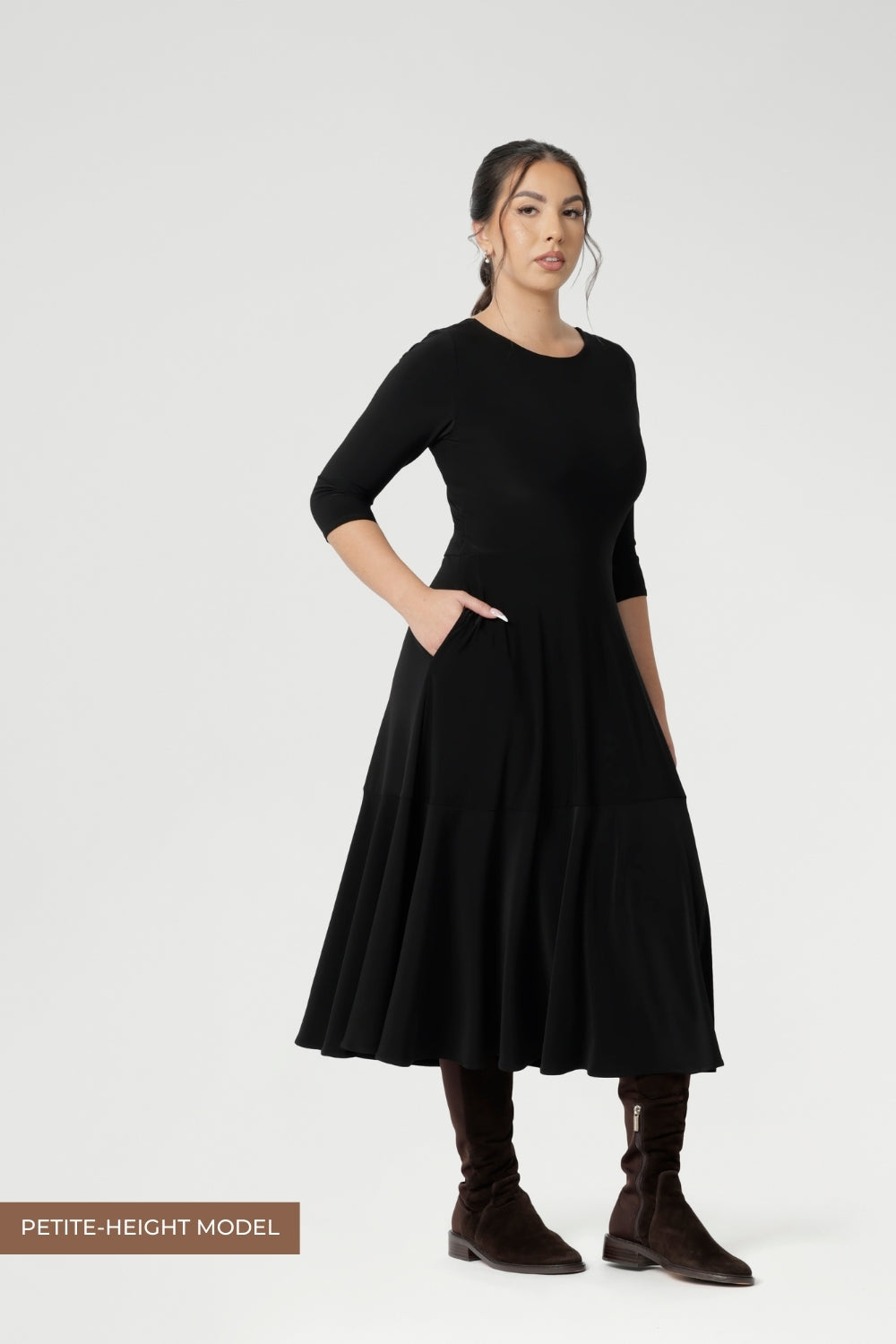 Petite height woman wears Bettina Reversible Dress in Black with petrol coloured jacket. Australian made Jersey fixed wrap dress features a V-neck style with pockets and midi length. Made in Australia with petite height and plus size women in mind. Available in sizes 8-24. 