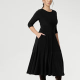 Petite height woman wears Bettina Reversible Dress in Black with petrol coloured jacket. Australian made Jersey fixed wrap dress features a V-neck style with pockets and midi length. Made in Australia with petite height and plus size women in mind. Available in sizes 8-24. 