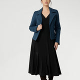 Petite height woman wears Bettina Reversible Dress in Black with petrol coloured jacket. Australian made Jersey fixed wrap dress features a V-neck style with pockets and midi length. Made in Australia with petite height and plus size women in mind. Available in sizes 8-24. 