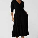 Size 16 woman wears a black reversible Bettina dress in black. V-neck style with pockets and midi length. Made in Australia for women size 8 - 24. 