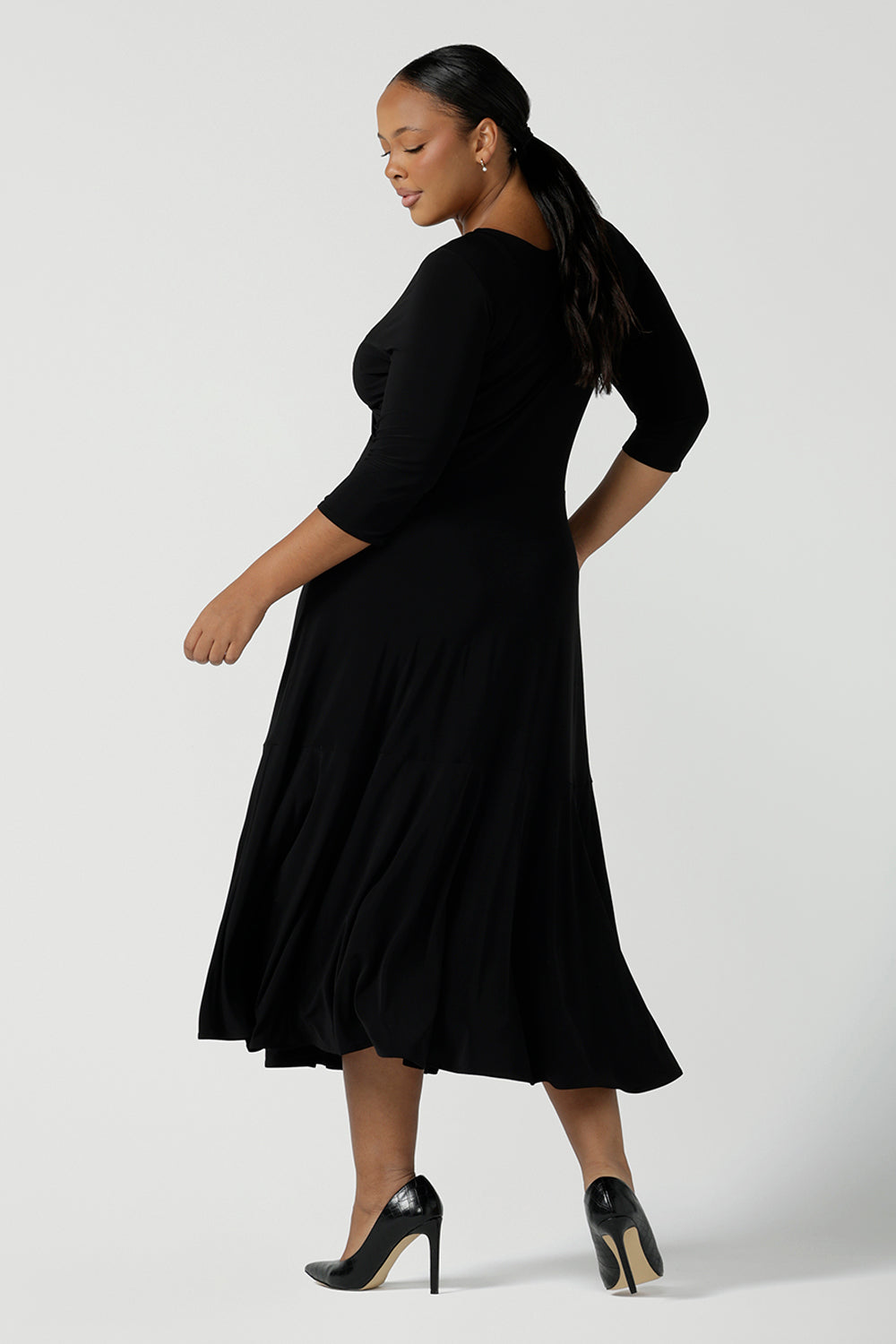 Back view of a size 16 woman wears a black reversible Bettina dress in black. V-neck style with pockets and midi length. Made in Australia for women size 8 - 24.