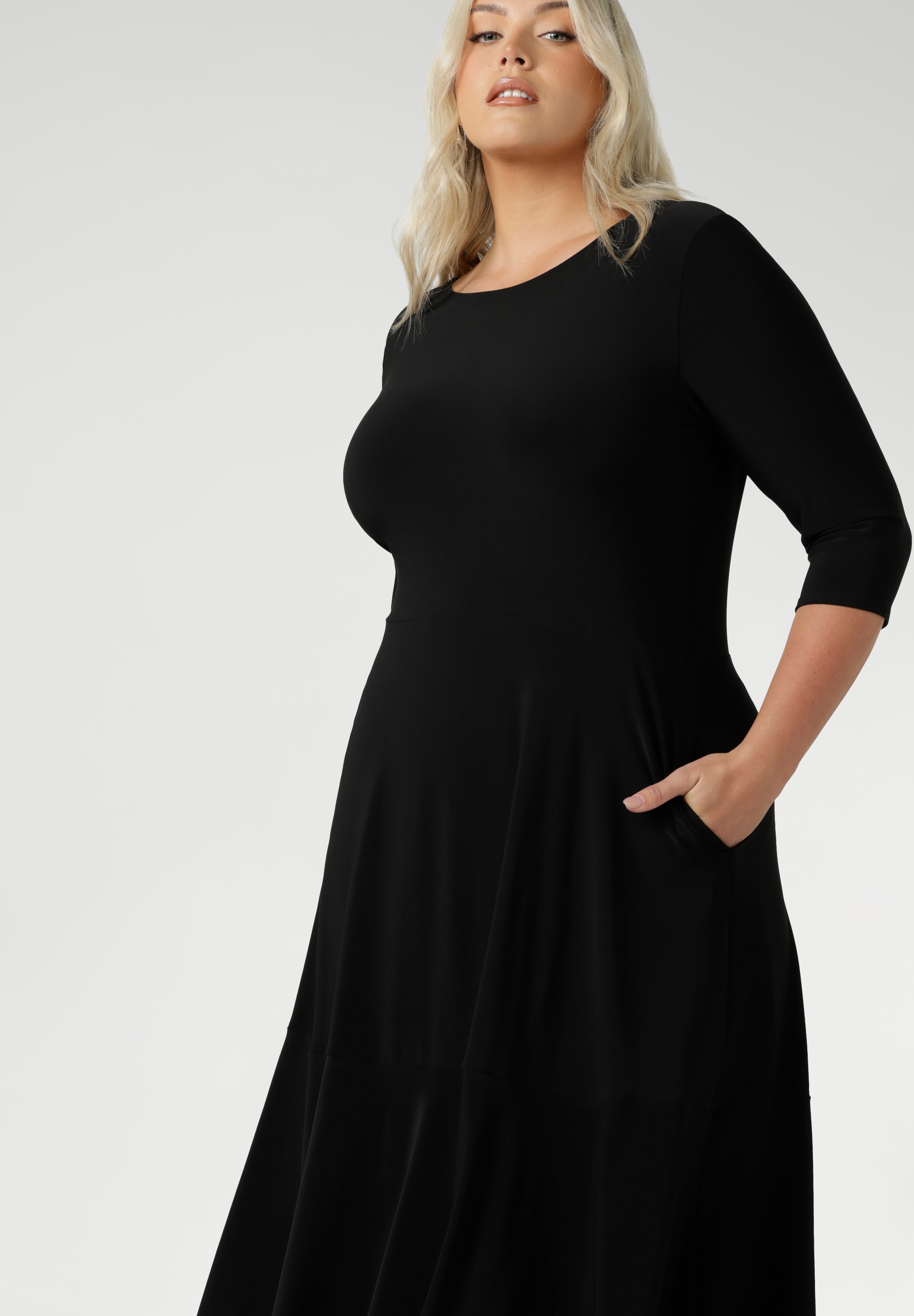 Size 18 woman wears a black reversible Bettina dress in black Jersey dress made in Australia. V-neck style with pockets and midi length. Made in Australia for women size 8 - 24. Reversible dress can be worn featuring boat neck or neck.