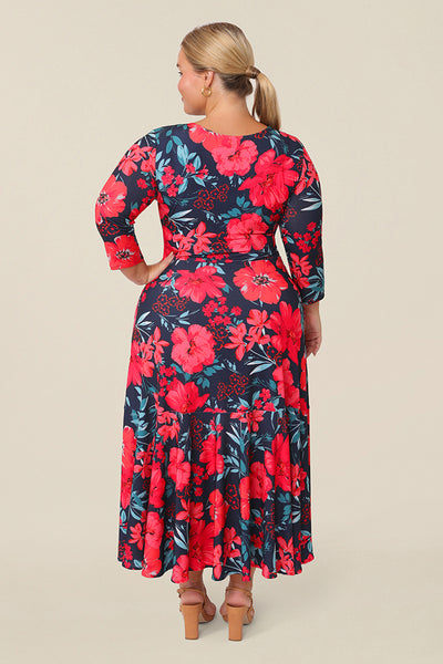 Back view of a curvy size 14 petite height woman wearing a reversible wrap dress with 3/4 sleeves. Featuring a midi-length skirt with ruffle hem and 3/4 length sleeves, this floral printed jersey dress wears well as a work dress or everyday dress. 