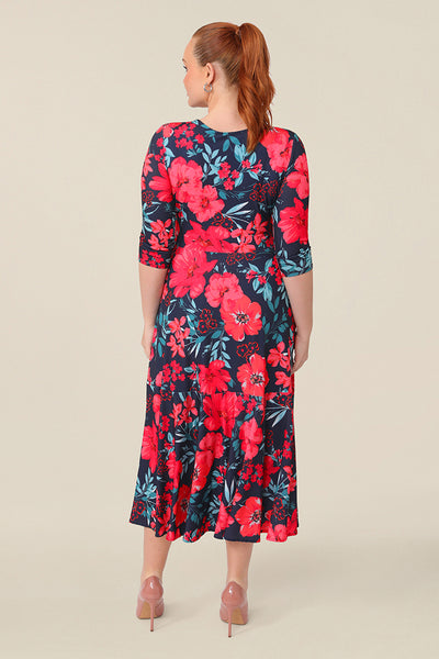 Back view of a curvy size 12 woman wearing a reversible wrap dress with 3/4 sleeves. Featuring a midi-length skirt with ruffle hem and 3/4 length sleeves, this floral printed jersey dress wears well as a work dress or everyday dress. 