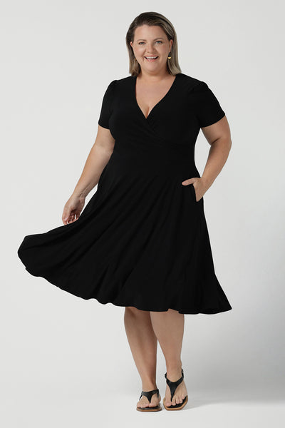 Size inclusive fashion for women.Curvy size 16 model wears black jersey dress in a fixed wrap style midi length. Comfortable corporate dress from work to weekend. Made in Australia for women size 8 - 24.