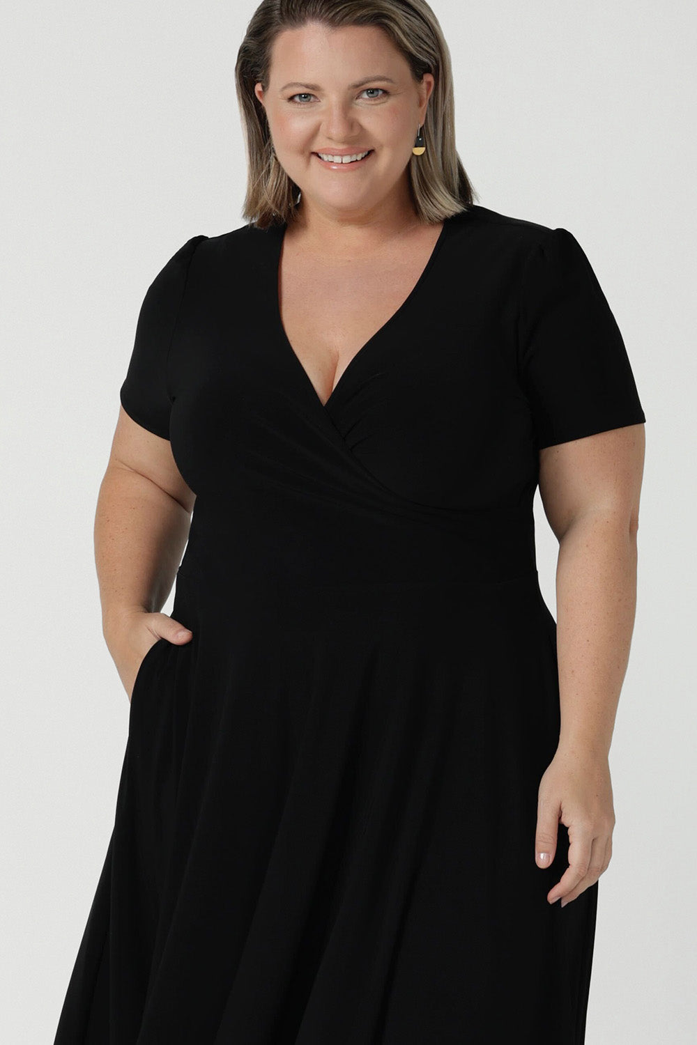 Close up of a size inclusive fashion for women.Curvy size 16 model wears black jersey dress in a fixed wrap style midi length. Comfortable corporate dress from work to weekend. Made in Australia for women size 8 - 24.