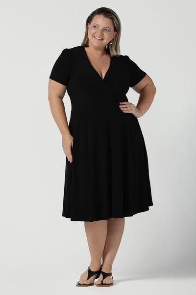 Size inclusive fashion for women.Curvy size 16 model wears black jersey dress in a fixed wrap style midi length. Comfortable corporate dress from work to weekend. Made in Australia for women size 8 - 24.