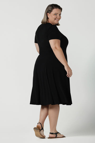 Back view of size inclusive fashion for women.Curvy size 16 model wears black jersey dress in a fixed wrap style midi length. Comfortable corporate dress from work to weekend. Made in Australia for women size 8 - 24.