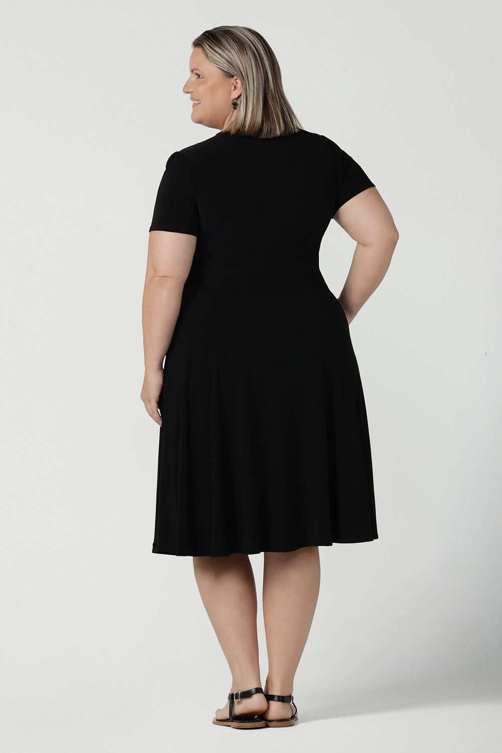 Back view of a size inclusive fashion for women.Curvy size 16 model wears black jersey dress in a fixed wrap style midi length. Comfortable corporate dress from work to weekend. Made in Australia for women size 8 - 24.
