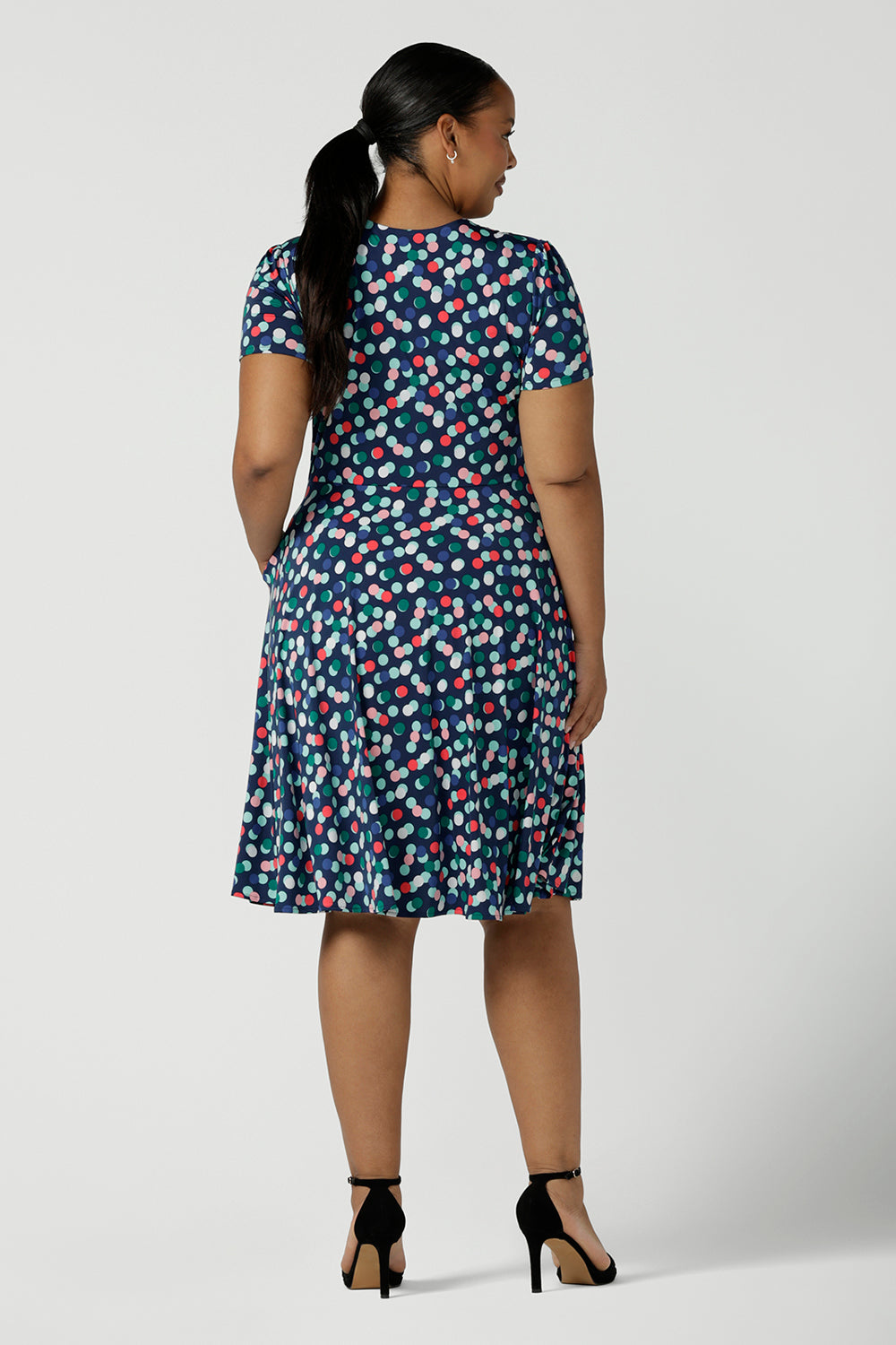 Back view of a curvy size 16 woman wears a Bubbles printed Jersey dress with a fixed wrap in a midi length. Styled back with a black heel. Perfect for work to weekend looks. Made in Australia for women size 8 - 24.