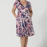 Size 12 women wears a fixed wrap dress with pockets, the perfect work to weekend of wedding guest dress. Comfortable and lightweight slinky jersey with a navy base and pink brush tones. Made in Australia for women size 8 - 24.