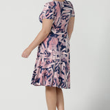 Back view of a size 12 women wearing a fixed wrap dress with pockets, the perfect work to weekend of wedding guest dress. Comfortable and lightweight slinky jersey with a navy base and pink brush tones. Made in Australia for women size 8 - 24.