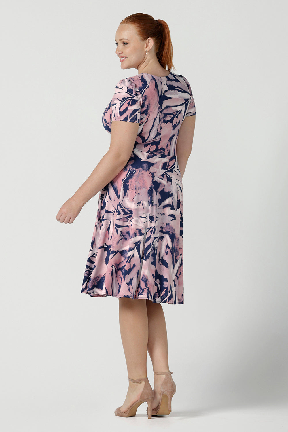 Back view of a size 12 women wearing a fixed wrap dress with pockets, the perfect work to weekend of wedding guest dress. Comfortable and lightweight slinky jersey with a navy base and pink brush tones. Made in Australia for women size 8 - 24.