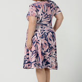 Back view of a size 18 curvy woman wearing the Alexis dress in Cantata. A navy base with pink brush strokes print. The perfect work to weekend or wedding guest outfit. Styled back with leather flats. Made in Australia for women size 8 - 24.