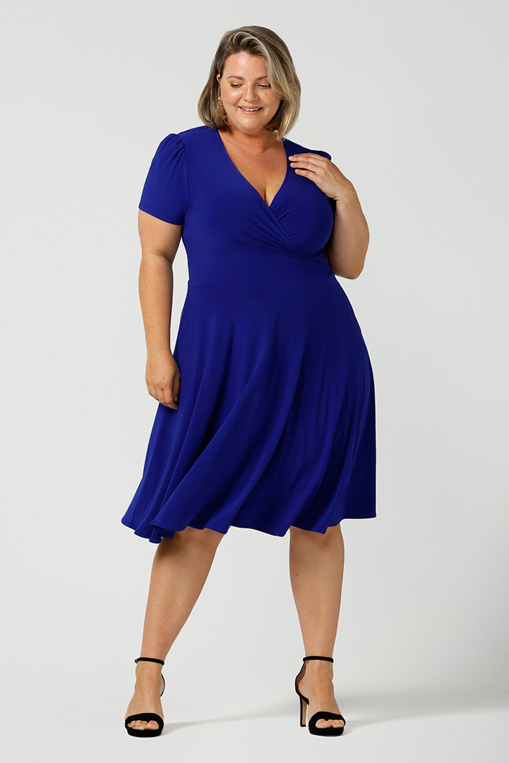 A size 18 woman wears a plus size jersey dress with short sleeves. In cobalt blue jersey, this dress is a good casual dress for weekend wear capsule wardrobes. Shop Australian-made wrap dresses for work online is sizes 8 to 24.